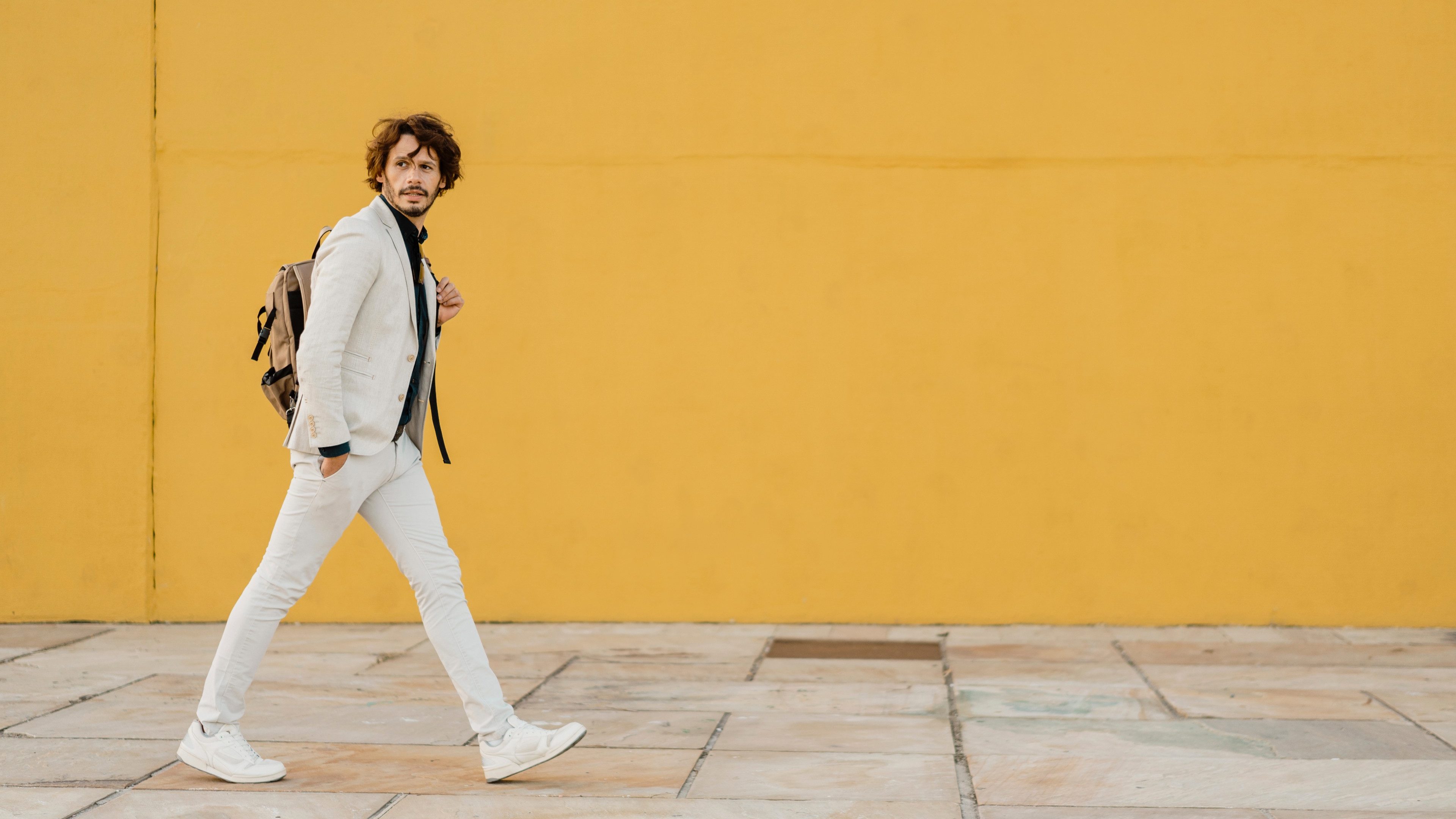 Portrait of walking businessman with backpack in front of yellow wall