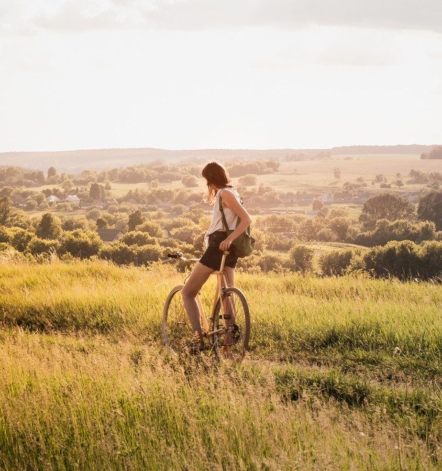 Young pretty female person with retro bike standing in a meadow on bright sunny afternoon in summer
