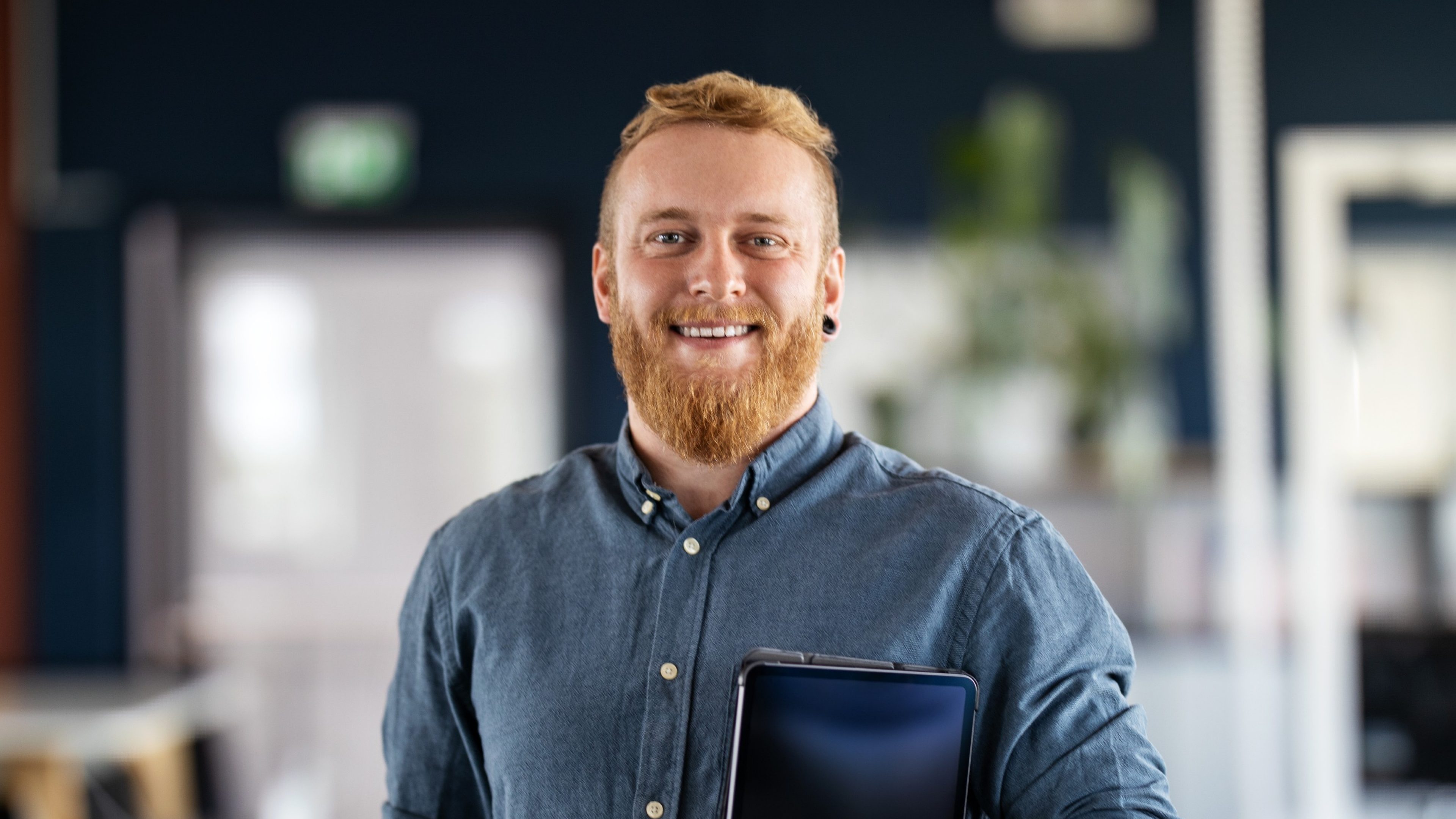 Portrait of a businessman with beard standing in office holding digital tablet. Confident male business executive in office looking at camera.