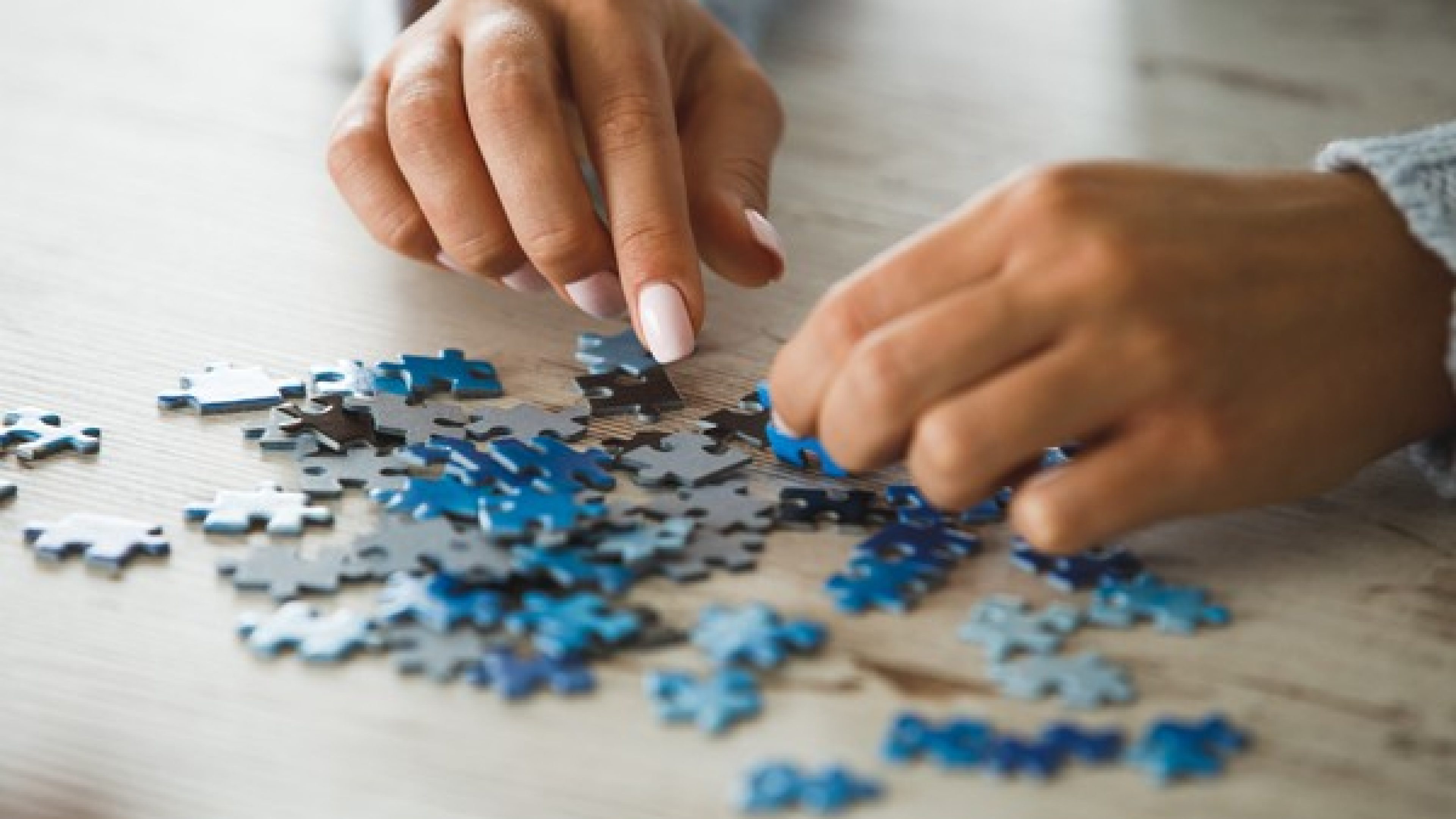 Close up of female hands playing with puzzle pieces on wooden table to spend free time in a healthy entertaining way.